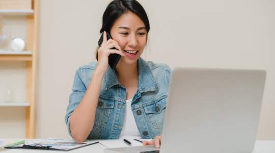 Woman talking on a cell phone while looking at a lap top