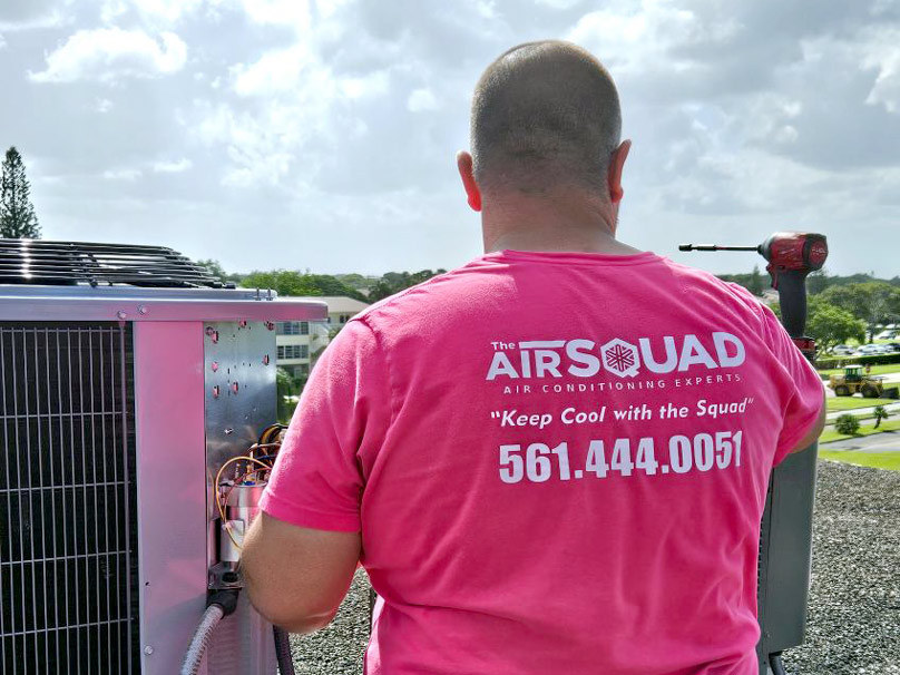 AC Repair Air Squad technician facing away and wearing a pink Air Squad t-shirt while repairing an air conditioner